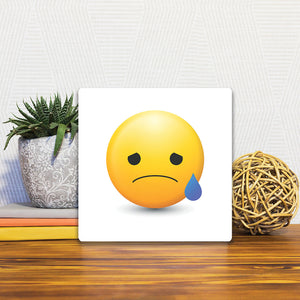 A Slidetile of the Sad Emoji sitting on a table.