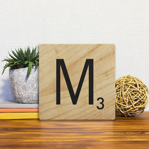 A Slidetile of the Letter M - Light Wood sitting on a table.